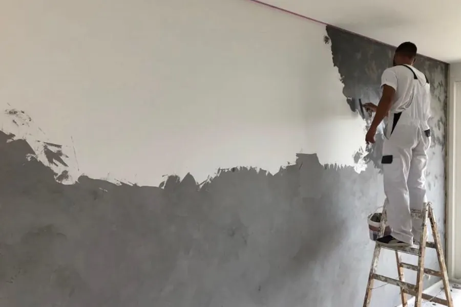 Peintre sur escabeau décapant l’ancien revêtement d’un mur intérieur